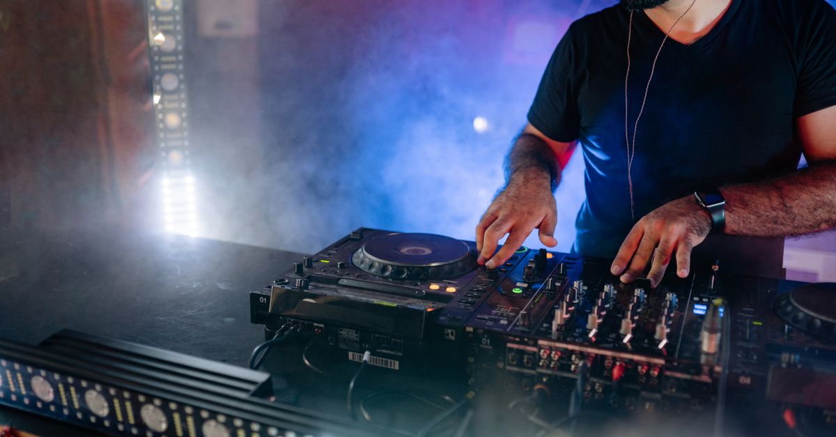 Energetic DJ performing live with mixing equipment in a colorful nightclub setting.