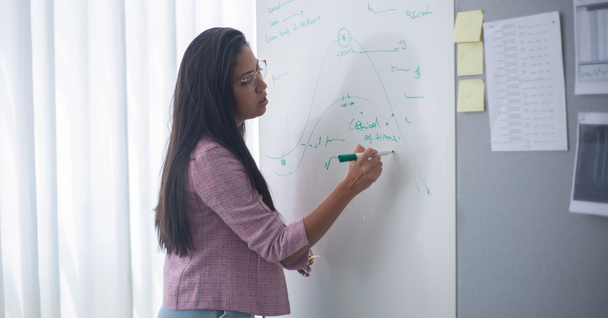 Businesswoman uses a whiteboard in office setting while brainstorming ideas.